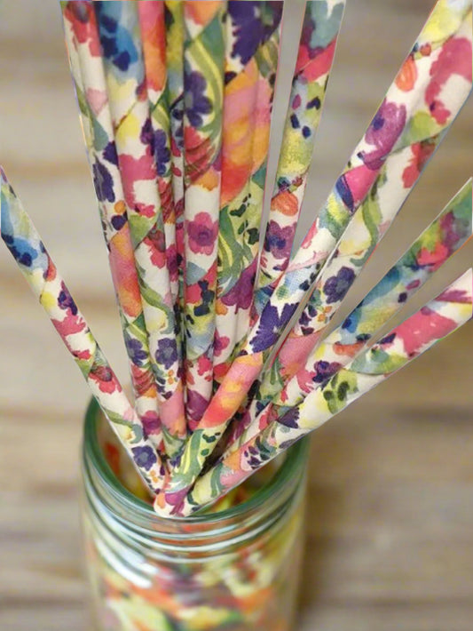 Colorful floral-patterned straws in a glass bowl on a white background