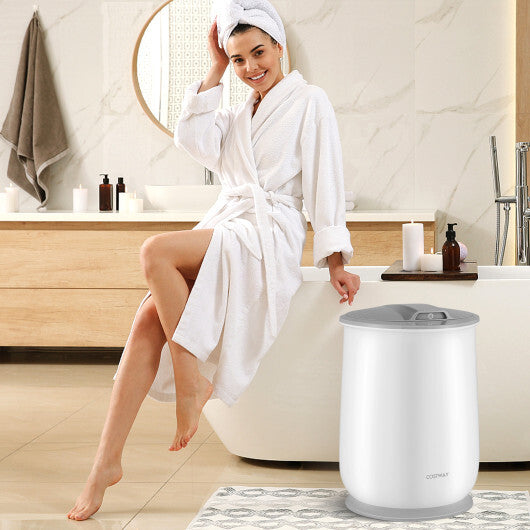 Woman in a white robe sitting on the edge of a bathtub with a white and gray appliance next to her.