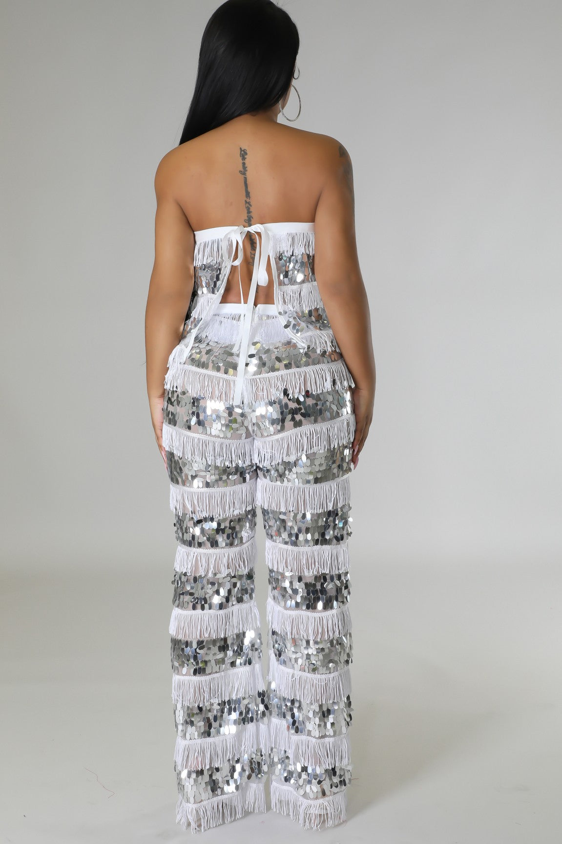 Woman wearing a white sequin jumpsuit on a plain background